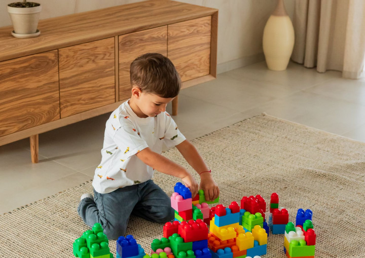Junge baut auf einem Teppich im Wohnzimmer mit bunten Klötzen