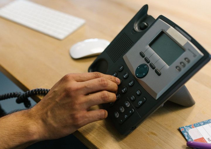 Eine Hand wählt eine Nummer an einem Telefon auf einem Schreibtisch
