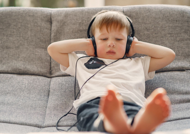 Ein Junge sitzt auf dem Sofa und hört mit Kopfhörern Musik